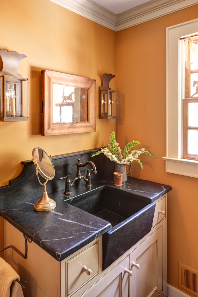 Klassisk inredning av ett litet badrum med dusch, med luckor med profilerade fronter, beige skåp, bänkskiva i täljsten, en dusch i en alkov, en toalettstol med separat cisternkåpa och orange väggar