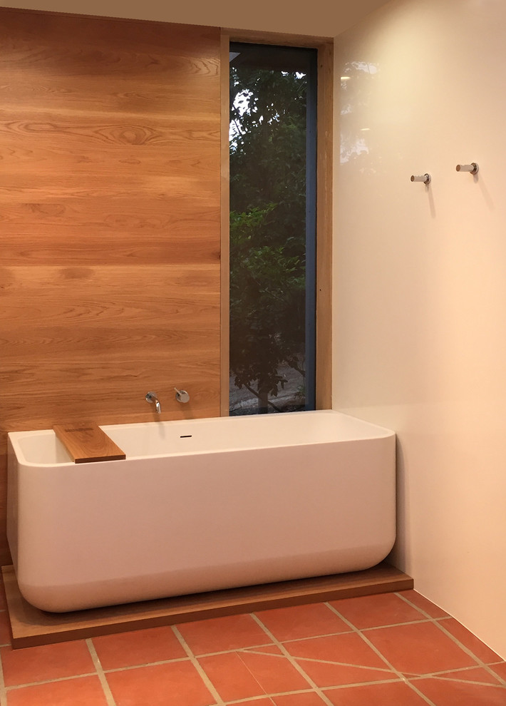 Réalisation d'une grande salle de bain minimaliste avec une baignoire indépendante, une douche ouverte, un carrelage blanc, des carreaux de porcelaine, un mur blanc, tomettes au sol, un sol marron et aucune cabine.
