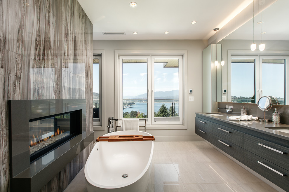 Modern inredning av ett grå grått badrum, med släta luckor, svarta skåp, ett fristående badkar, brun kakel, grå väggar, ett undermonterad handfat och grått golv