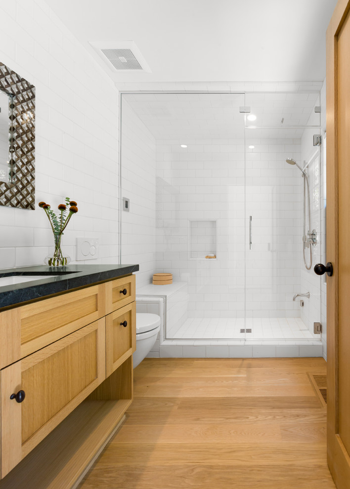 Foto på ett mellanstort retro badrum med dusch, med skåp i shakerstil, skåp i ljust trä, en dusch i en alkov, en vägghängd toalettstol, vit kakel, keramikplattor, vita väggar, ljust trägolv, ett undermonterad handfat, bänkskiva i täljsten, gult golv och dusch med gångjärnsdörr