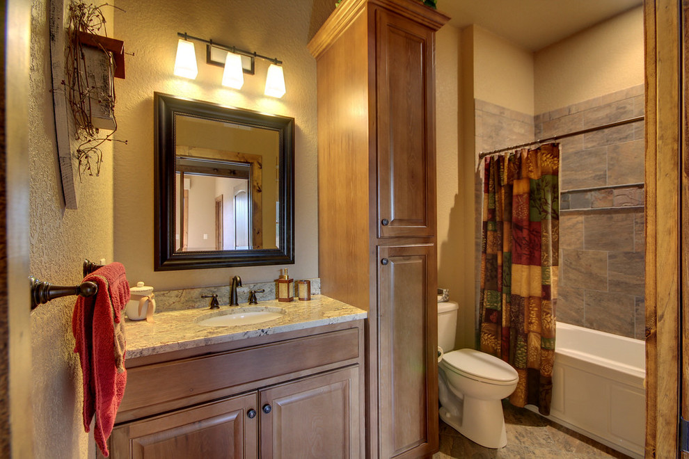 This is an example of a medium sized classic bathroom in Atlanta with raised-panel cabinets, medium wood cabinets, an alcove bath, a shower/bath combination, a one-piece toilet, brown tiles, stone tiles, beige walls, ceramic flooring, a submerged sink and granite worktops.