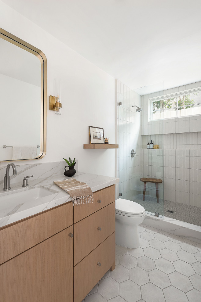 Lantlig inredning av ett vit vitt badrum, med släta luckor, skåp i ljust trä, en dusch i en alkov, vit kakel, vita väggar, ett undermonterad handfat, vitt golv och med dusch som är öppen