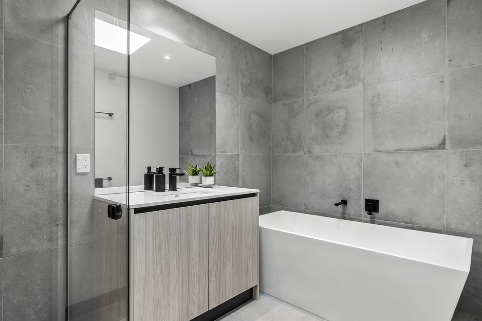 Photo of a modern bathroom in Geelong with flat-panel cabinets, light wood cabinets, a freestanding bath, a corner shower, grey tiles, cement tiles, cement flooring, a built-in sink, engineered stone worktops, grey floors, a hinged door and white worktops.