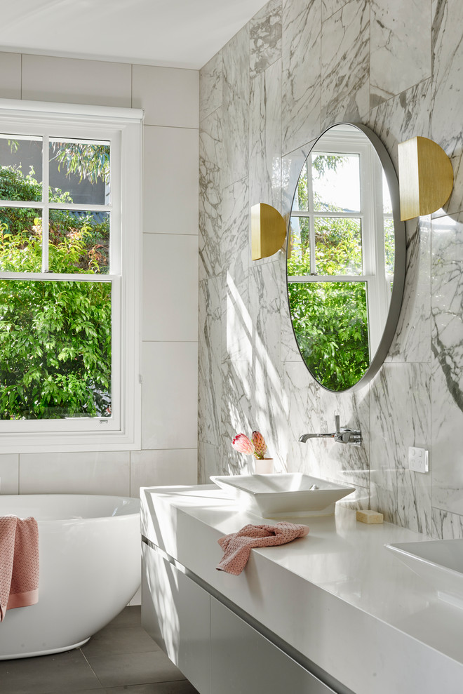 Modernes Badezimmer mit flächenbündigen Schrankfronten, grauen Schränken, freistehender Badewanne, weißen Fliesen, Aufsatzwaschbecken, grauem Boden und weißer Waschtischplatte in Geelong