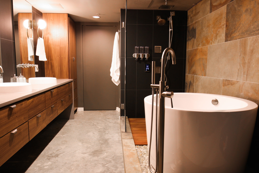 ヒューストンにある高級な小さなトランジショナルスタイルのおしゃれなマスターバスルーム (フラットパネル扉のキャビネット、中間色木目調キャビネット、和式浴槽、オープン型シャワー、ビデ、黒いタイル、石タイル、グレーの壁、コンクリートの床、一体型シンク、珪岩の洗面台、グレーの床、開き戸のシャワー、グレーの洗面カウンター) の写真