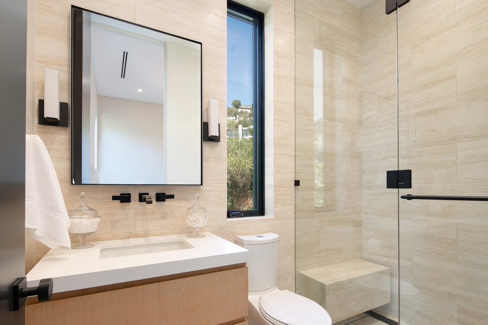 Cette photo montre une grande douche en alcôve tendance en bois clair avec un placard à porte plane, WC à poser, une cabine de douche à porte battante, un carrelage beige, un lavabo encastré et un plan de toilette blanc.
