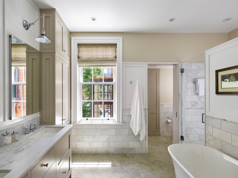 Traditional ensuite bathroom in Philadelphia with shaker cabinets, a freestanding bath, marble tiles, limestone flooring, a submerged sink, marble worktops, a hinged door, beige cabinets, white tiles, beige walls, grey floors and white worktops.