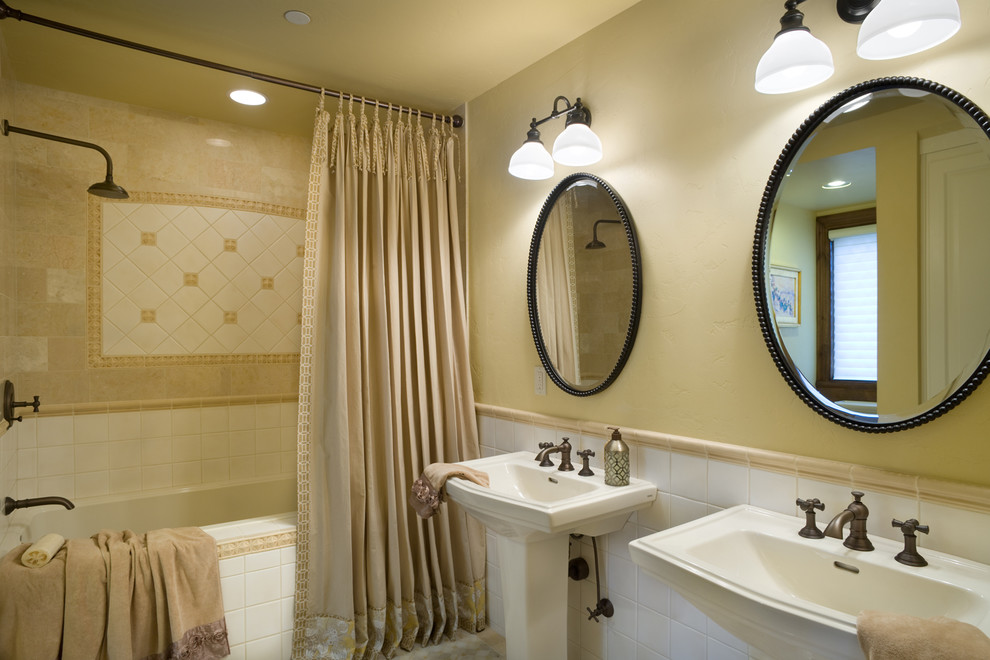 Modelo de cuarto de baño tradicional con lavabo con pedestal, bañera empotrada, combinación de ducha y bañera y baldosas y/o azulejos beige