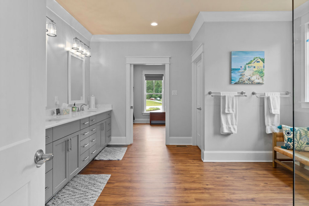 Design ideas for a large coastal ensuite bathroom in Raleigh with shaker cabinets, grey cabinets, a corner shower, a two-piece toilet, grey walls, vinyl flooring, a submerged sink, solid surface worktops, brown floors, a hinged door, white worktops, a shower bench, double sinks and a built in vanity unit.