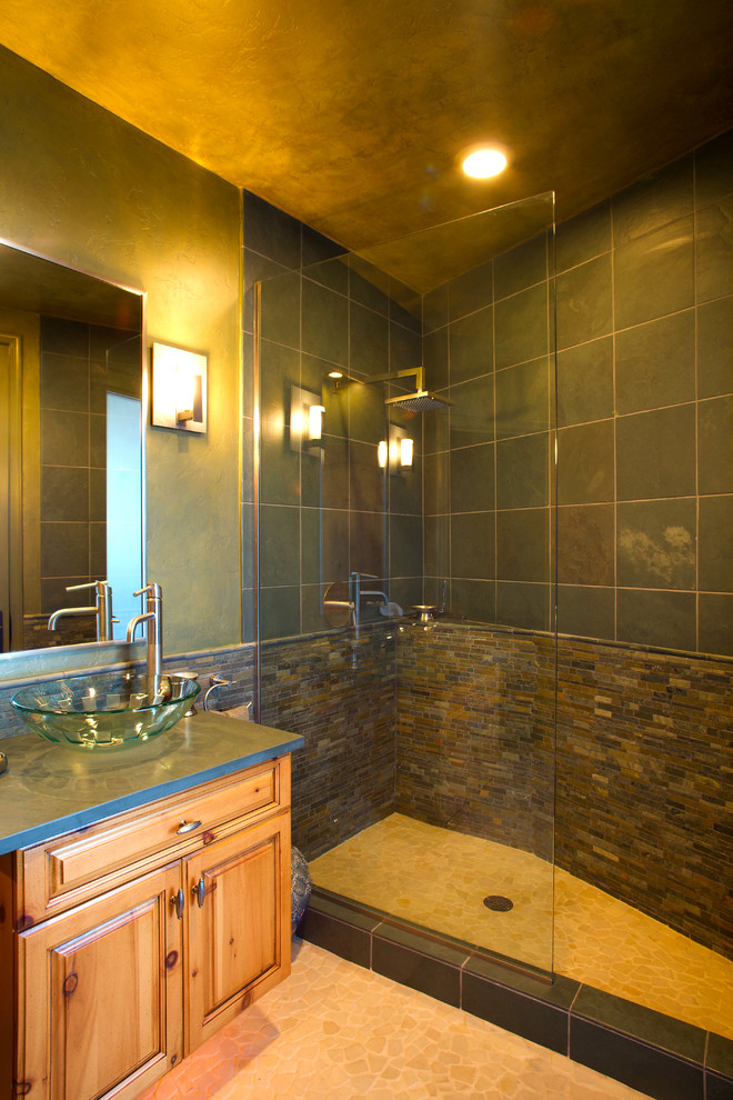 Exemple d'une salle d'eau tendance en bois clair avec une vasque, un placard avec porte à panneau surélevé, un carrelage vert, un carrelage de pierre, un mur vert, une douche d'angle et un sol en galet.