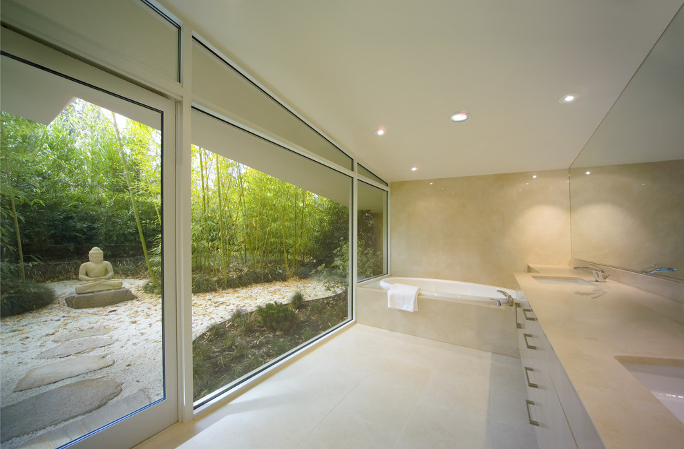 Идея дизайна: большая главная ванная комната в стиле модернизм с врезной раковиной, плоскими фасадами, белыми фасадами, накладной ванной, бежевыми стенами, полом из известняка и столешницей из известняка