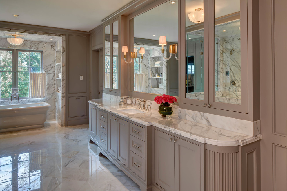 Inredning av ett klassiskt en-suite badrum, med grå skåp, ett fristående badkar, marmorkakel, grå väggar, marmorgolv, ett undermonterad handfat, marmorbänkskiva, vitt golv och luckor med profilerade fronter