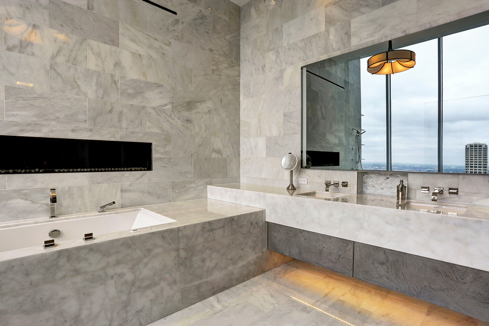 Cette image montre une grande salle de bain principale design avec un placard à porte plane, des portes de placard grises, une baignoire encastrée, un carrelage gris, du carrelage en marbre, un mur gris, un lavabo encastré, un plan de toilette en marbre, un sol en marbre et un sol gris.