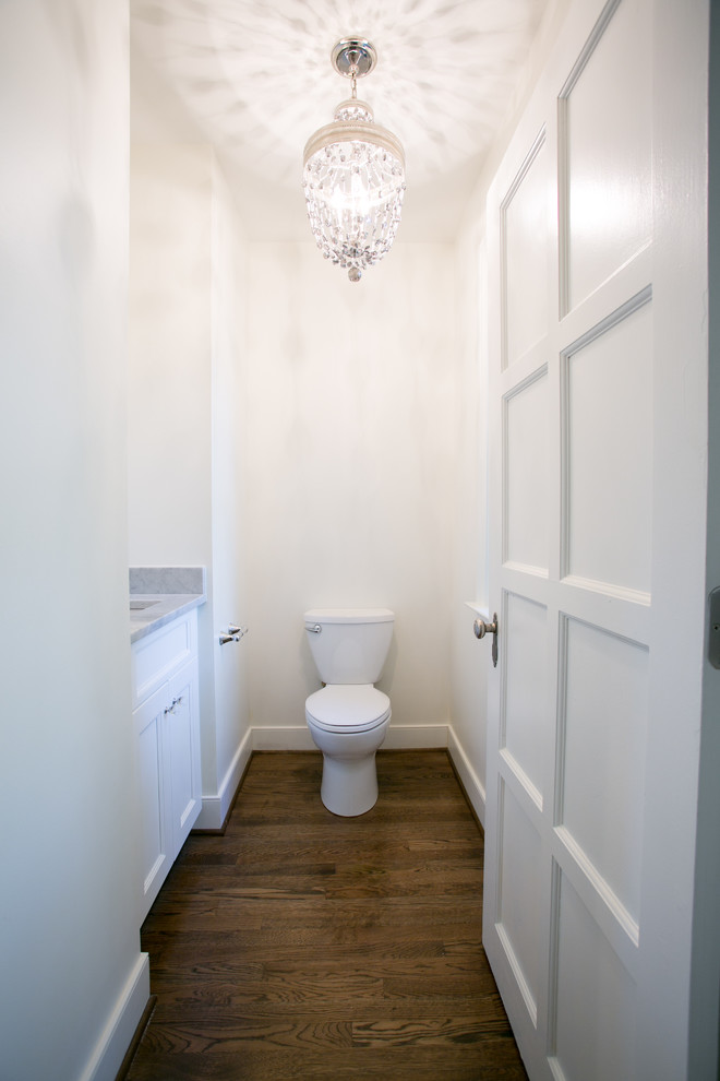 Cette photo montre un grand WC et toilettes chic avec un carrelage blanc, un placard à porte shaker, des portes de placard blanches, WC à poser, un mur blanc, parquet foncé et un lavabo encastré.