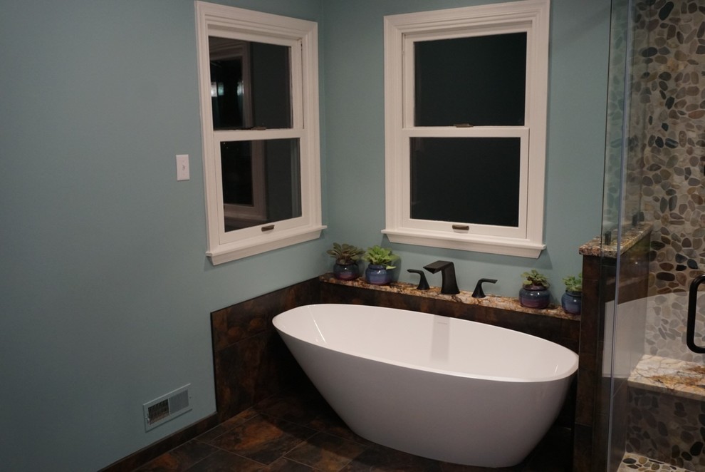 Cette photo montre une grande salle de bain principale moderne en bois brun avec un placard avec porte à panneau surélevé, une baignoire indépendante, une douche d'angle, un carrelage gris, du carrelage en ardoise, un mur bleu, un sol en ardoise, un lavabo encastré, un plan de toilette en quartz, un sol gris et une cabine de douche à porte battante.