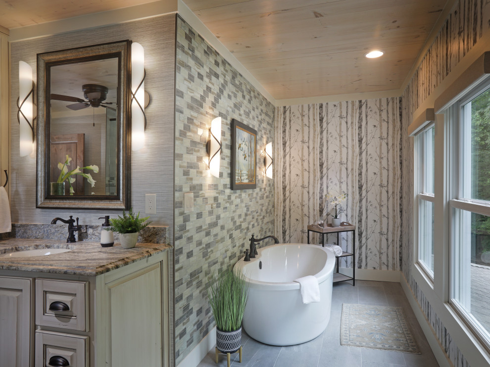 Example of a mountain style gray tile gray floor, single-sink and wallpaper freestanding bathtub design in Atlanta with raised-panel cabinets, light wood cabinets, multicolored walls, an undermount sink, brown countertops and a built-in vanity