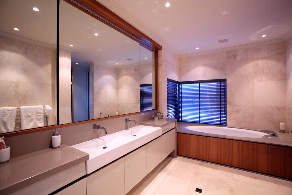 Cette image montre une salle de bain vintage avec un placard à porte plane, des portes de placard blanches, une baignoire encastrée, un carrelage beige, un mur beige, un lavabo posé et un plan de toilette en granite.