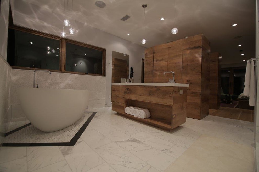 Modern inredning av ett stort en-suite badrum, med ett avlångt handfat, möbel-liknande, skåp i mellenmörkt trä, bänkskiva i betong, ett fristående badkar, en dusch i en alkov, en toalettstol med hel cisternkåpa, vit kakel, stenkakel, grå väggar och marmorgolv