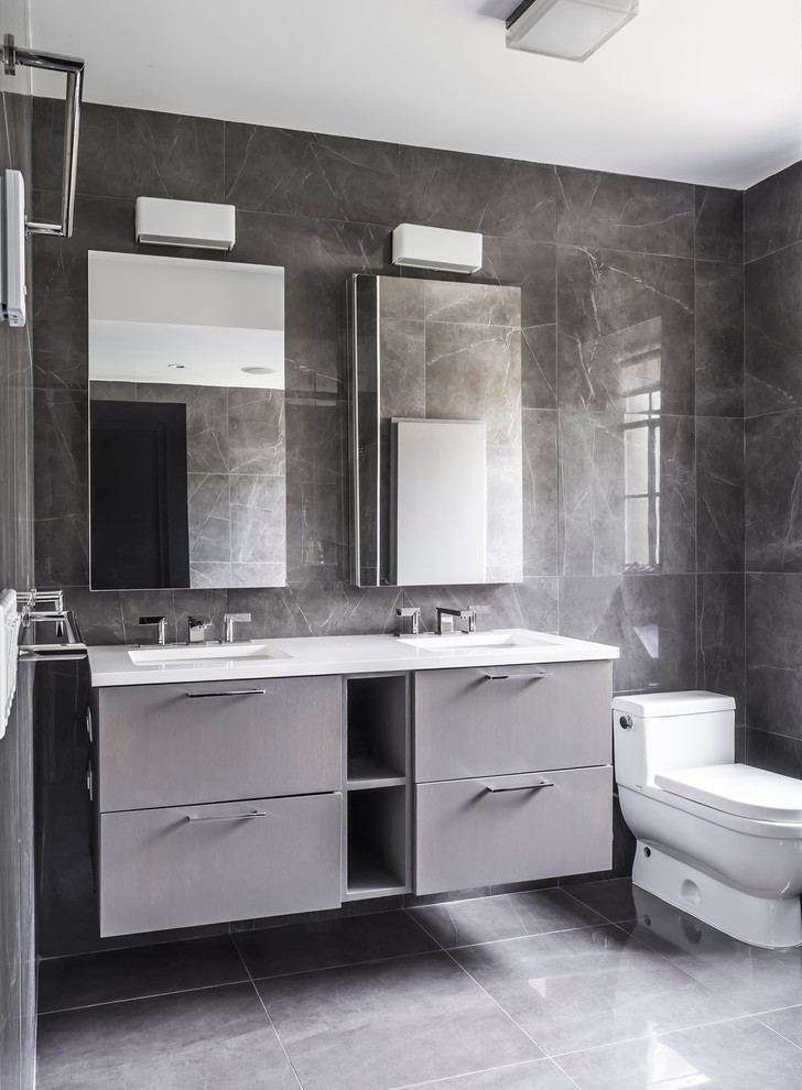 Modern inredning av ett mellanstort badrum med dusch, med släta luckor, grå skåp, en vägghängd toalettstol, grå kakel, klinkergolv i keramik, marmorkakel, grå väggar och bänkskiva i akrylsten