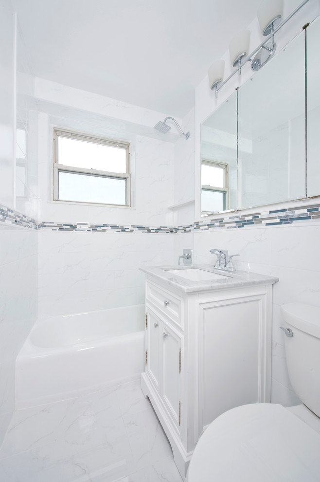 Bild på ett litet funkis en-suite badrum, med möbel-liknande, ett badkar i en alkov, en dusch/badkar-kombination, en toalettstol med separat cisternkåpa, vit kakel, stenkakel, vita väggar, klinkergolv i porslin, ett undermonterad handfat, marmorbänkskiva och vita skåp