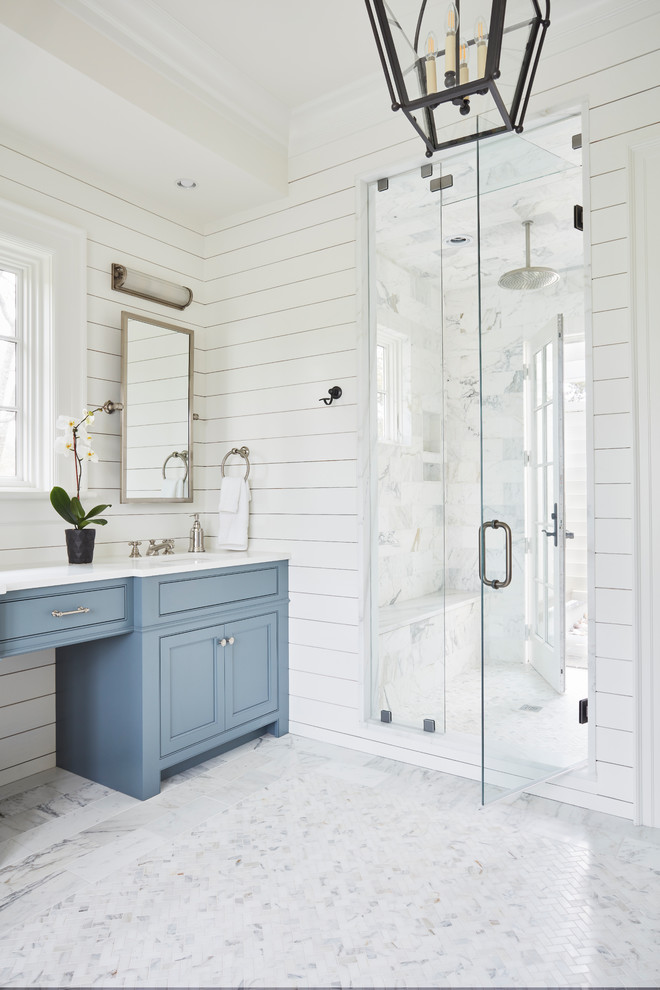 Стильный дизайн: ванная комната в стиле кантри с фасадами с утопленной филенкой, синими фасадами, отдельно стоящей ванной, душем без бортиков, белой плиткой, мраморной плиткой, белыми стенами, мраморным полом, накладной раковиной, мраморной столешницей, белым полом, душем с распашными дверями и белой столешницей - последний тренд