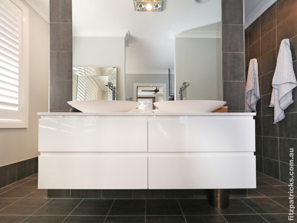 Modern inredning av ett badrum, med vita skåp, grå kakel, grå väggar, grått golv och med dusch som är öppen