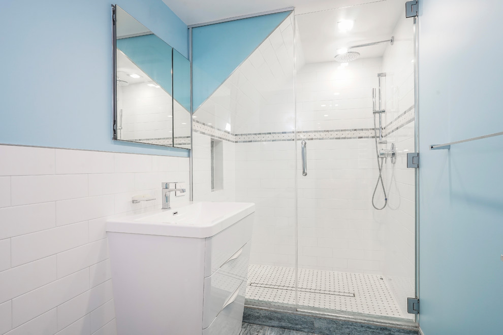 Inredning av ett modernt stort vit vitt badrum för barn, med släta luckor, vita skåp, en dusch i en alkov, en vägghängd toalettstol, vit kakel, tunnelbanekakel, blå väggar, marmorgolv, ett nedsänkt handfat, bänkskiva i onyx, blått golv och dusch med gångjärnsdörr