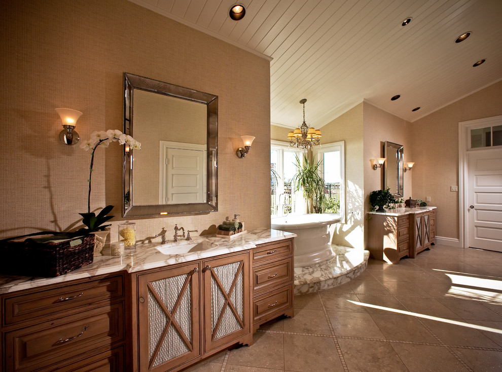 Inredning av ett klassiskt stort badrum, med ett nedsänkt handfat, luckor med profilerade fronter, skåp i mellenmörkt trä, marmorbänkskiva och ett fristående badkar