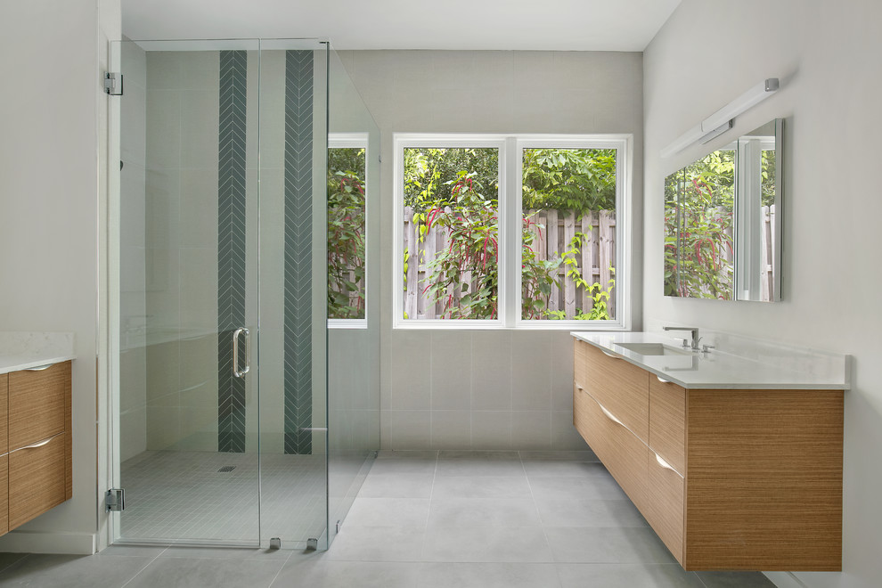Corner shower - mid-sized contemporary master white tile and porcelain tile porcelain tile and gray floor corner shower idea in Tampa with flat-panel cabinets, medium tone wood cabinets, a two-piece toilet, white walls, an undermount sink, quartz countertops, a hinged shower door and white countertops