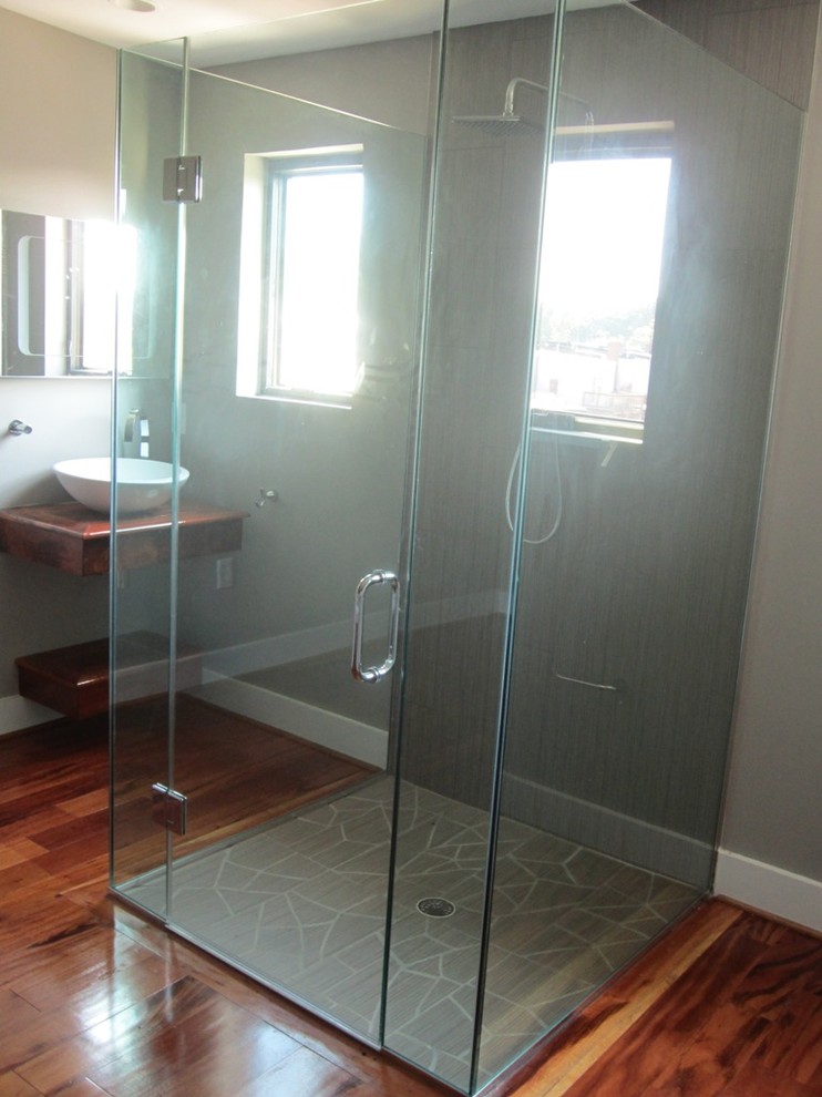 Photo of a medium sized contemporary bathroom in Houston with a wall-mounted sink, wooden worktops, a freestanding bath, a built-in shower, a one-piece toilet, ceramic tiles, grey walls and medium hardwood flooring.