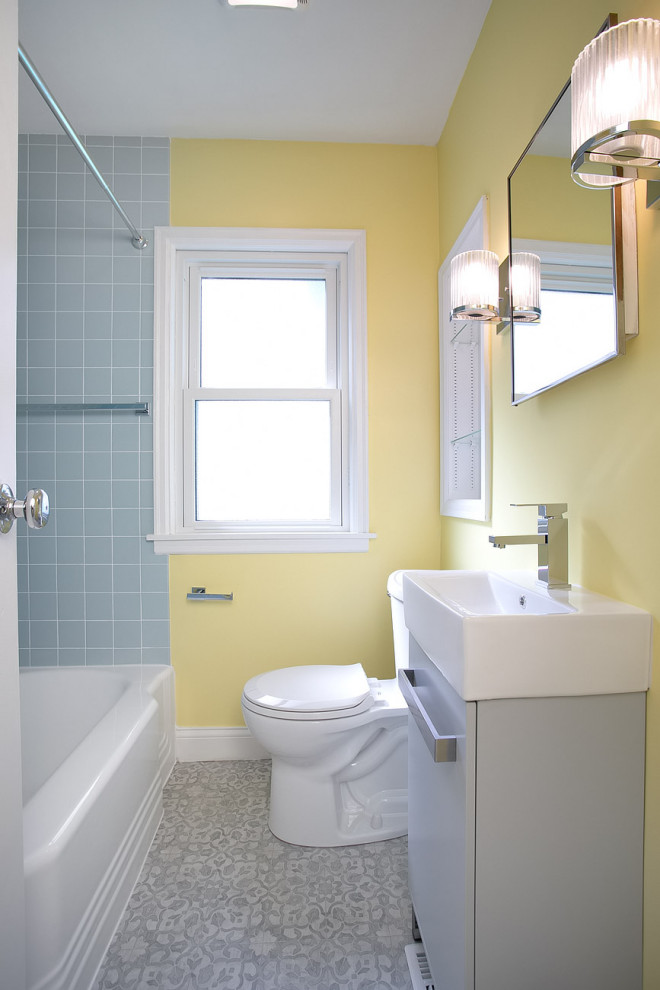 Aménagement d'une petite salle de bain principale rétro avec un placard à porte plane, des portes de placard grises, une baignoire posée, un combiné douche/baignoire, WC à poser, un carrelage bleu, des carreaux de céramique, un mur jaune, un sol en vinyl, un plan de toilette en surface solide, un sol gris, une cabine de douche avec un rideau, un plan de toilette blanc, meuble simple vasque et meuble-lavabo encastré.