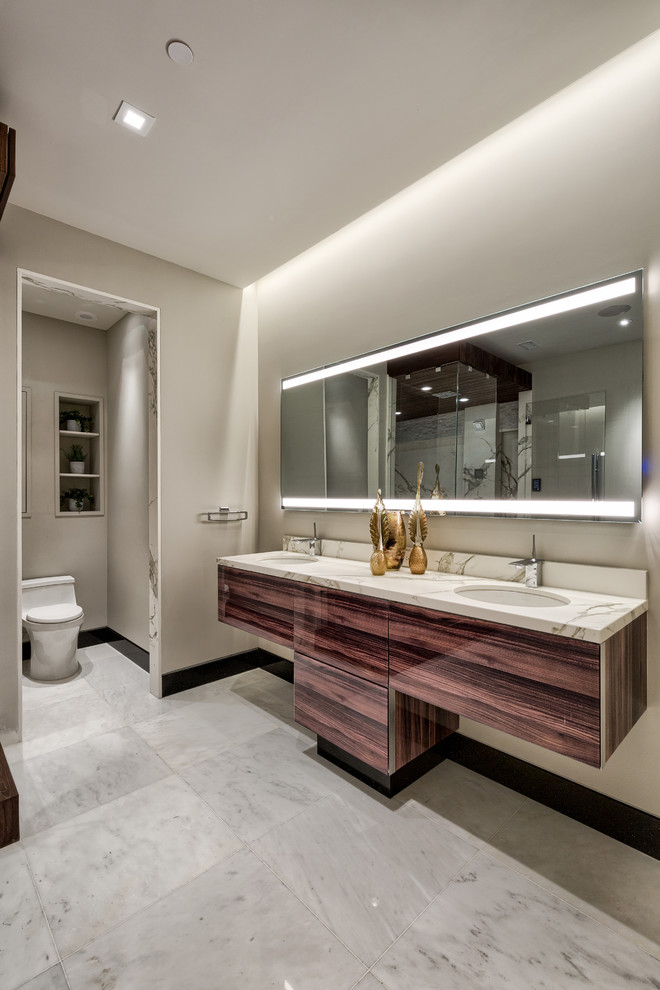 Large minimalist master marble floor and white floor bathroom photo in Other with flat-panel cabinets, dark wood cabinets, a one-piece toilet, gray walls, an undermount sink, marble countertops, a hinged shower door and white countertops
