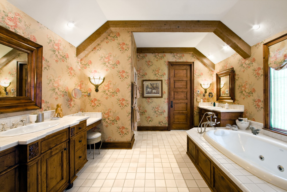Modelo de cuarto de baño de estilo de casa de campo con lavabo encastrado, puertas de armario de madera en tonos medios, encimera de azulejos, bañera encastrada, baldosas y/o azulejos blancos y armarios con paneles empotrados