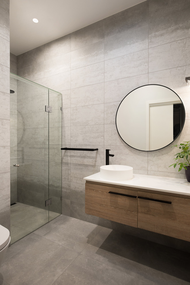 Mid-sized trendy master gray tile and ceramic tile ceramic tile and gray floor alcove shower photo in Melbourne with flat-panel cabinets, dark wood cabinets, a wall-mount toilet, gray walls, a console sink, solid surface countertops and a hinged shower door