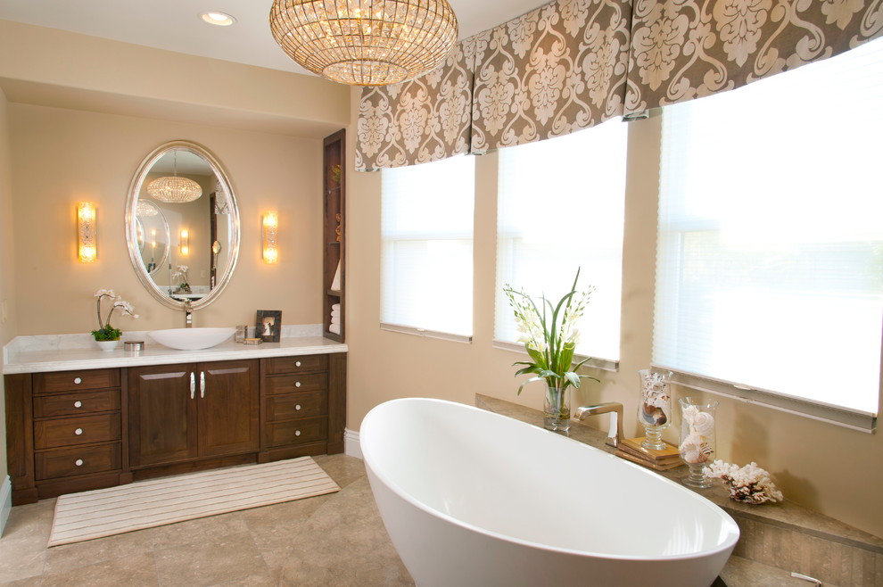 Inspiration for a large transitional master beige tile and mosaic tile limestone floor freestanding bathtub remodel in San Diego with a vessel sink, raised-panel cabinets, dark wood cabinets, marble countertops, a one-piece toilet and beige walls