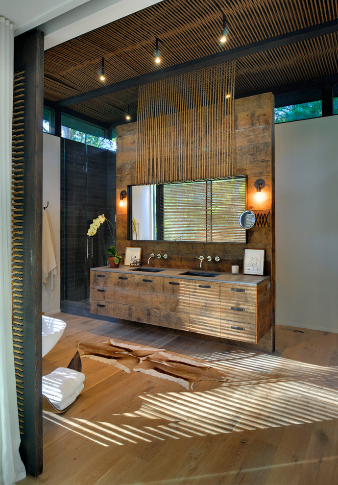 Exempel på ett modernt badrum, med skåp i slitet trä, ett fristående badkar och svart kakel