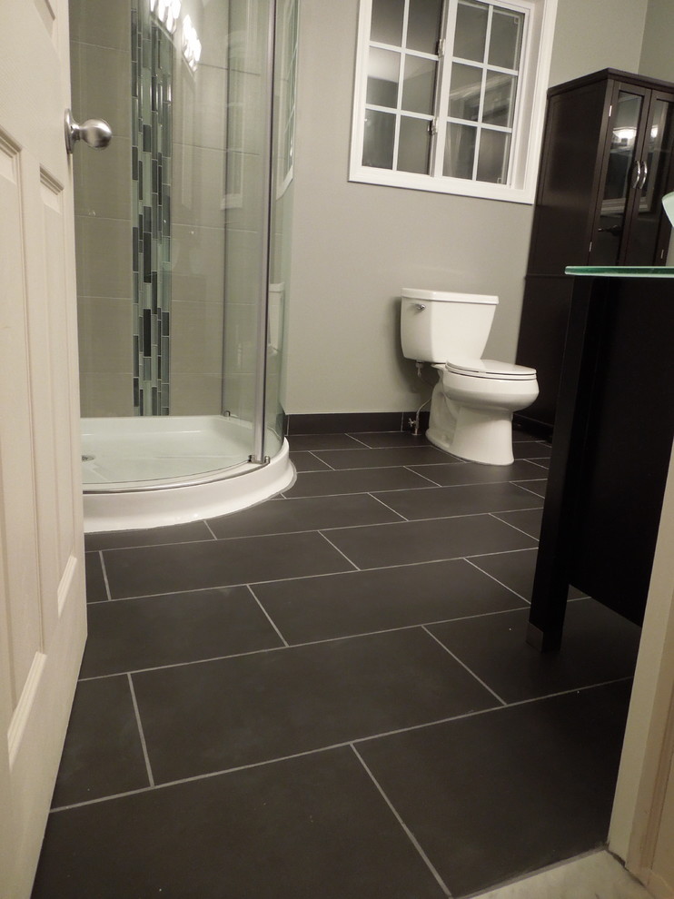 Exemple d'une salle de bain principale moderne en bois foncé de taille moyenne avec WC séparés, des carreaux de porcelaine, un mur gris, un sol en carrelage de porcelaine, un placard à porte vitrée, une douche d'angle, un carrelage gris, une vasque et un plan de toilette en verre.