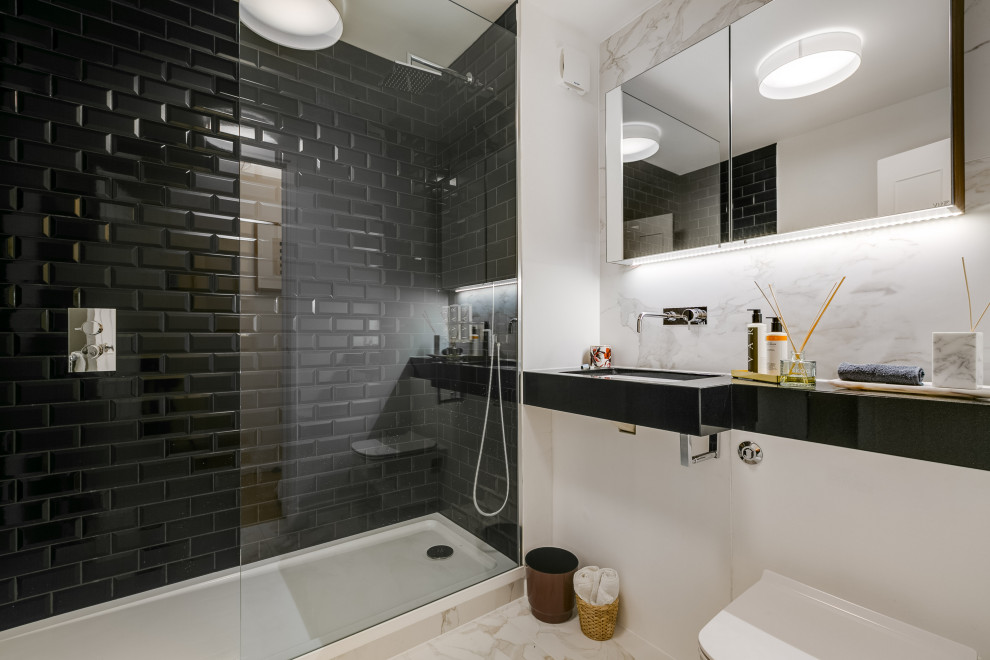 На фото: ванная комната среднего размера в современном стиле с черными фасадами, душем в нише, инсталляцией, черной плиткой, плиткой кабанчик, белыми стенами, душевой кабиной, монолитной раковиной, бежевым полом и черной столешницей