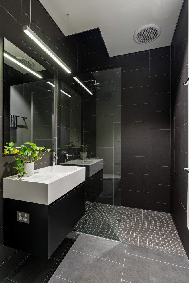 Пример оригинального дизайна: ванная комната среднего размера в современном стиле с плоскими фасадами, черными фасадами, черной плиткой, керамогранитной плиткой, полом из керамогранита, душевой кабиной, монолитной раковиной, серым полом, открытым душем и белой столешницей