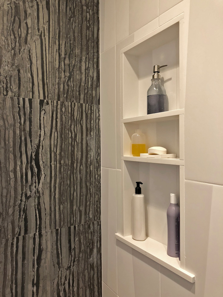 Inredning av ett modernt mellanstort grå grått badrum med dusch, med luckor med glaspanel, grå skåp, en kantlös dusch, en vägghängd toalettstol, svart och vit kakel, stenkakel, vita väggar, klinkergolv i porslin, ett integrerad handfat, bänkskiva i glas, grått golv och dusch med gångjärnsdörr
