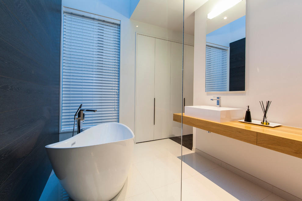 Medium sized contemporary ensuite bathroom in Christchurch with flat-panel cabinets, light wood cabinets, a freestanding bath, a corner shower, a one-piece toilet, black and white tiles, white walls, ceramic flooring and wooden worktops.