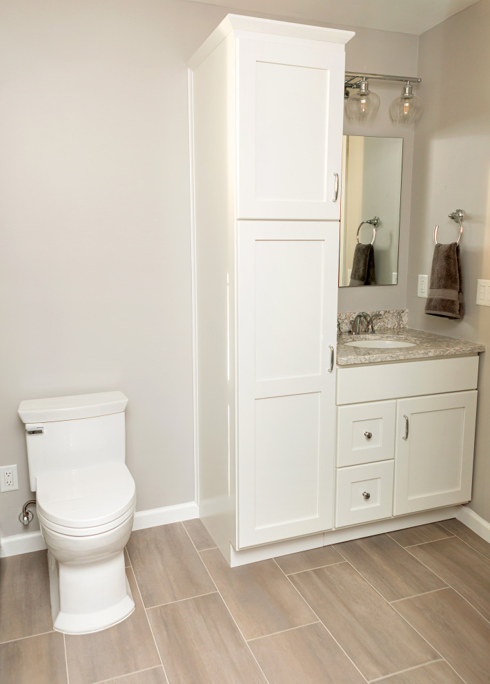 Example of a mid-sized transitional porcelain tile alcove shower design in New York with shaker cabinets, white cabinets, a one-piece toilet, gray walls, an undermount sink, quartz countertops, a hinged shower door and gray countertops