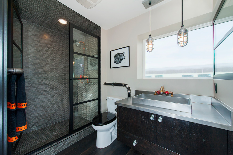 This is an example of an industrial shower room bathroom in Calgary with flat-panel cabinets, an alcove shower, a two-piece toilet, mosaic tiles, beige walls, dark hardwood flooring, a vessel sink, stainless steel worktops, black cabinets, grey tiles and a hinged door.