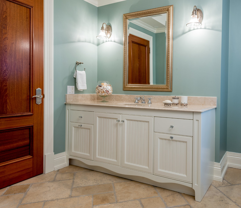 Idée de décoration pour une salle de bain tradition de taille moyenne avec un placard avec porte à panneau encastré, des portes de placard blanches, un mur bleu, un sol en calcaire, un lavabo encastré et un plan de toilette en marbre.