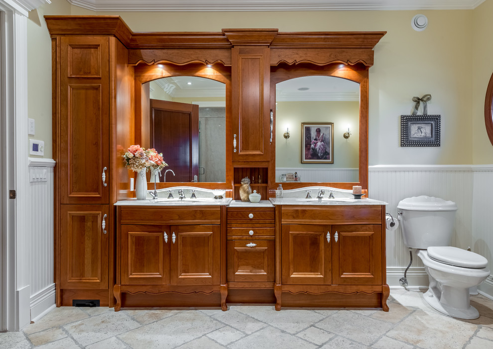 Exempel på ett mellanstort klassiskt en-suite badrum, med luckor med infälld panel, skåp i mellenmörkt trä, en toalettstol med separat cisternkåpa, gula väggar, kalkstensgolv, ett undermonterad handfat och marmorbänkskiva