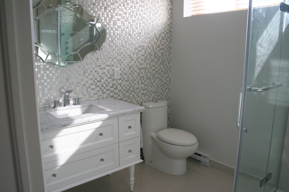 Modelo de cuarto de baño ecléctico pequeño con armarios tipo mueble, puertas de armario blancas, encimera de mármol, baldosas y/o azulejos grises, ducha esquinera, sanitario de una pieza, lavabo bajoencimera, paredes grises y suelo de baldosas de porcelana