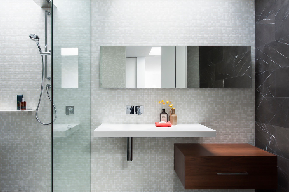 Foto di una stanza da bagno minimalista di medie dimensioni con lavabo integrato, consolle stile comò, ante in legno scuro, top in superficie solida, vasca freestanding, doccia aperta, WC sospeso, piastrelle di vetro e pavimento in marmo