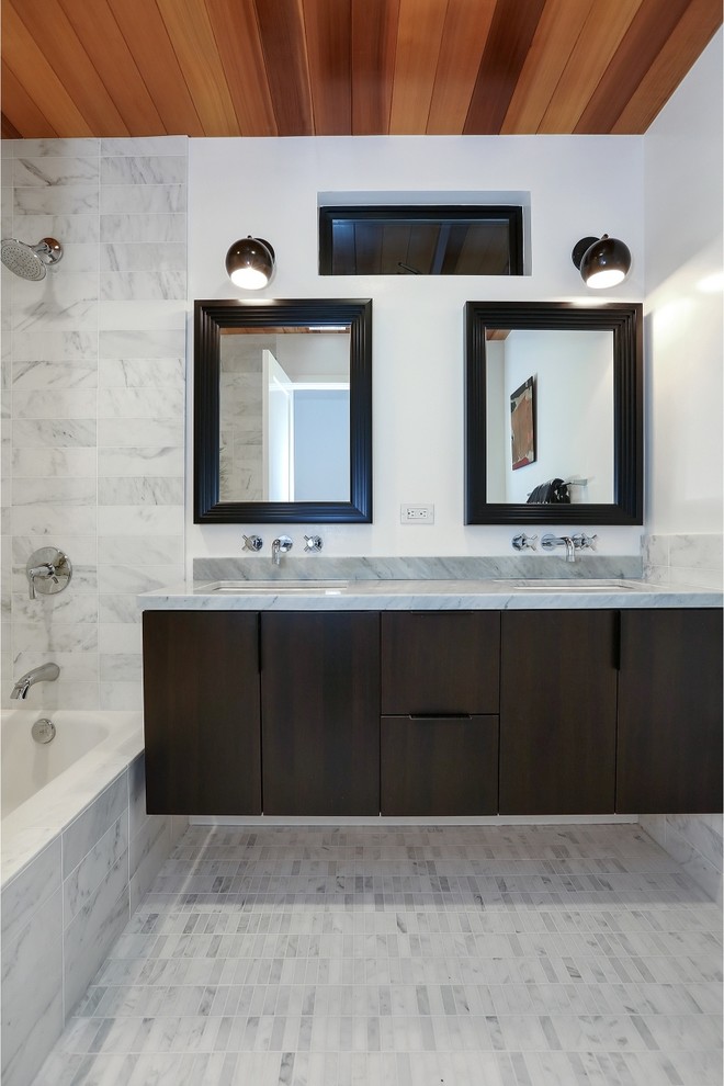 На фото: ванная комната в современном стиле с врезной раковиной, плоскими фасадами, темными деревянными фасадами, ванной в нише, белой плиткой, каменной плиткой, белыми стенами, полом из мозаичной плитки и серой столешницей