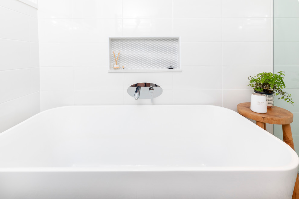 На фото: главная ванная комната среднего размера в современном стиле с фасадами с выступающей филенкой, светлыми деревянными фасадами, отдельно стоящей ванной, угловым душем, раздельным унитазом, белой плиткой, керамической плиткой, белыми стенами, полом из керамогранита, настольной раковиной, столешницей из искусственного кварца, разноцветным полом, душем с распашными дверями и разноцветной столешницей