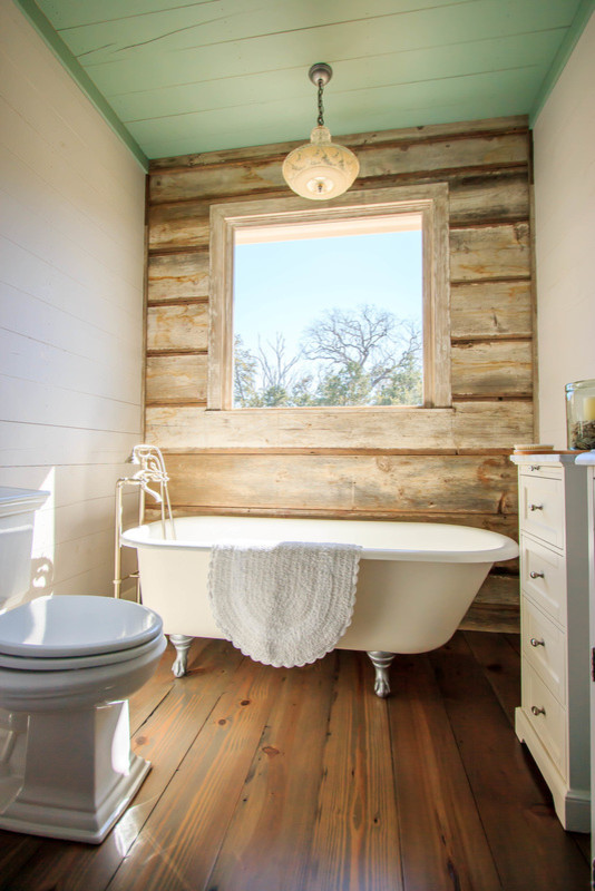 Bild på ett mellanstort lantligt badrum med dusch, med luckor med infälld panel, vita skåp, ett badkar med tassar, en toalettstol med separat cisternkåpa, vita väggar, mörkt trägolv och brunt golv